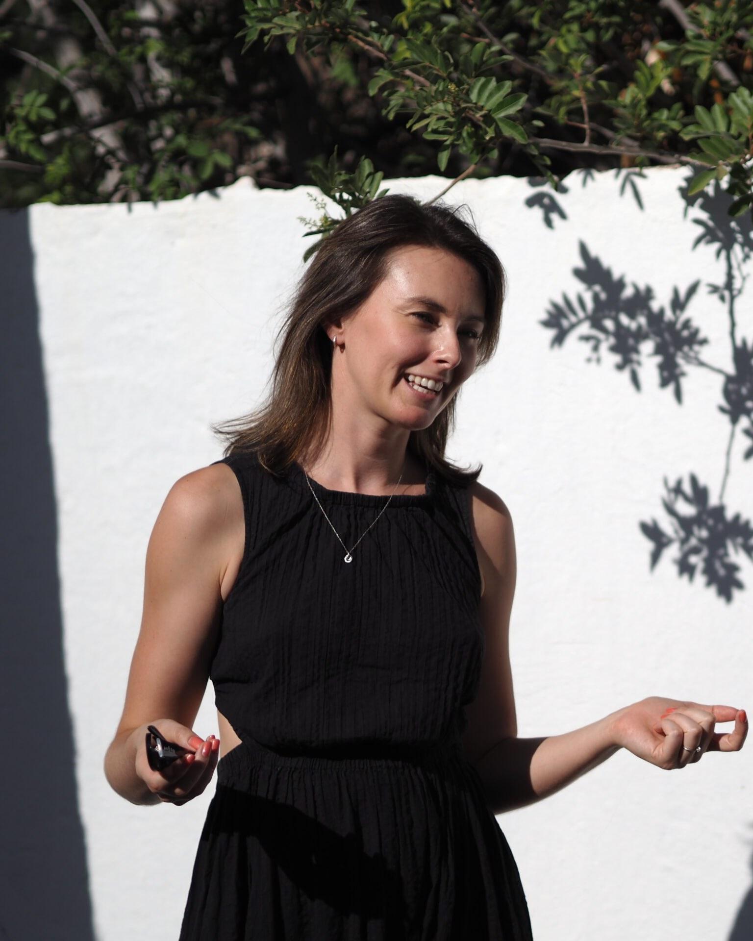 Becci smiling in front of a white wall with leaf shadows