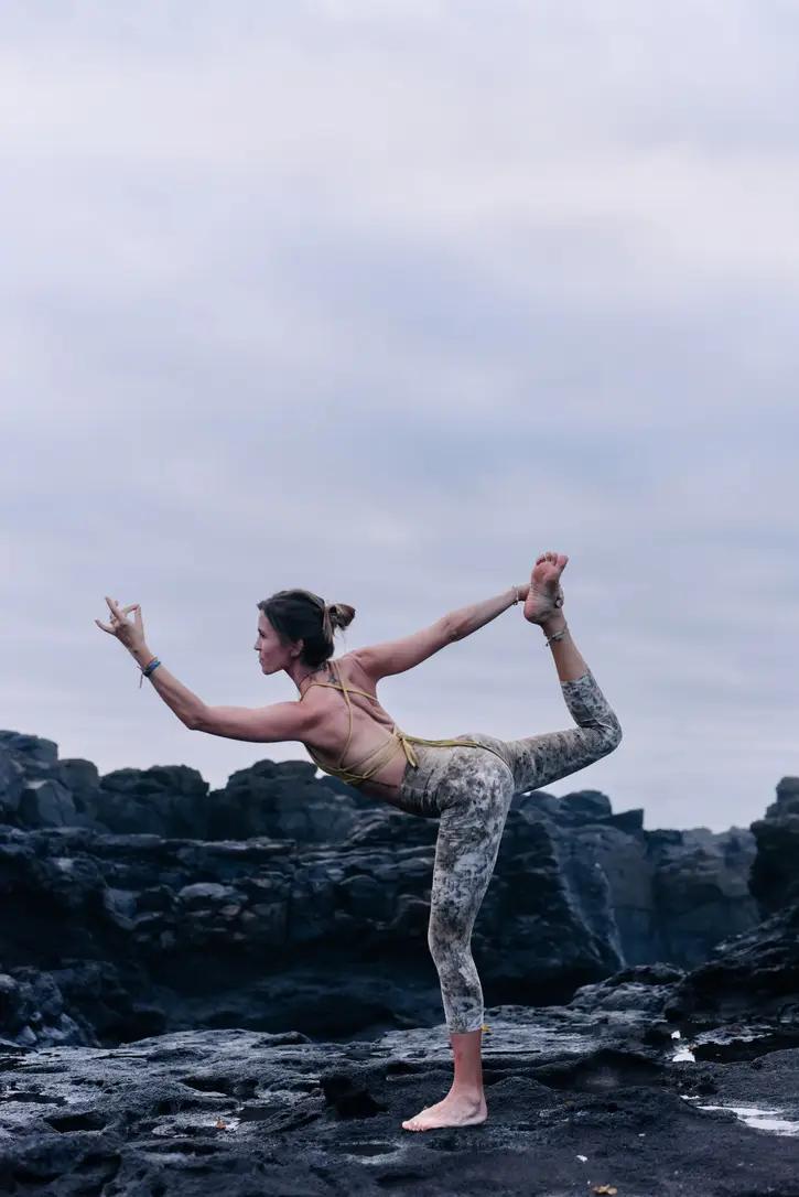 Larissa in a standing yoga pose on dark rocks by the sea